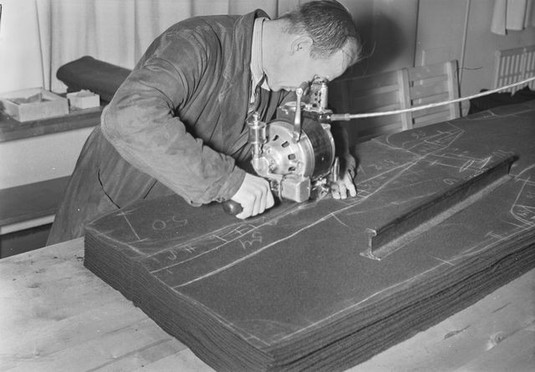 Mies käyttää sähköllä toimivaa kankaan leikkauskonetta. 1939. Kuva: Aarne Pietinen Oy. Museovirasto. CC BY 4.0.
