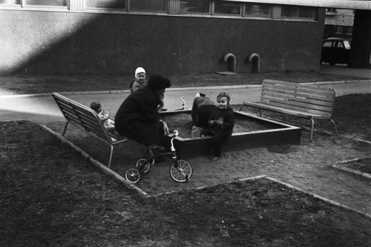 Lapsia hiekkalaatikolla aikuisen valvonnassa ja pieni polkupyörä. Helsinki, Neljäs linja, 1970. Kuva: Eeva Rista. Helsingin kaupunginmuseo.
