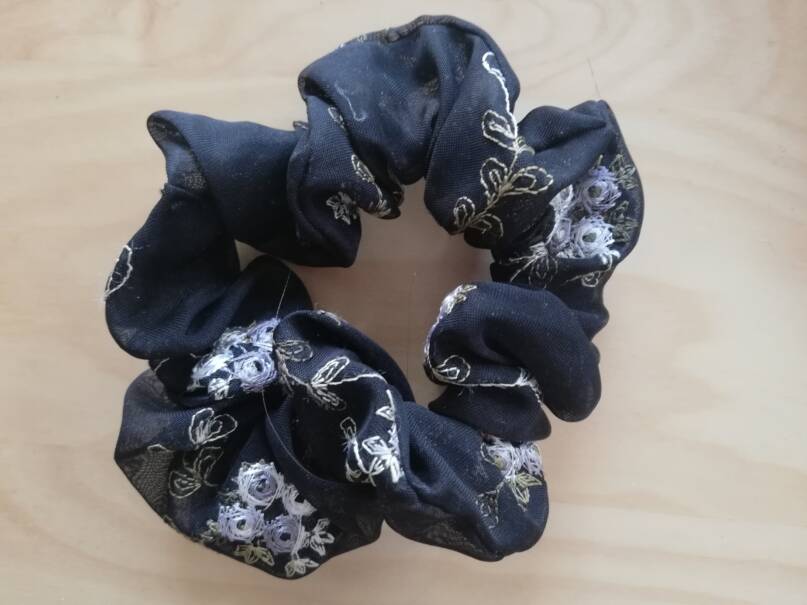 Kuvassa laivastonsininen ja kukilla kuvioitu hiusdonitsi eli scrunchie. Hiuksia hellävaraisemmin kohteleva hiuslenkki.