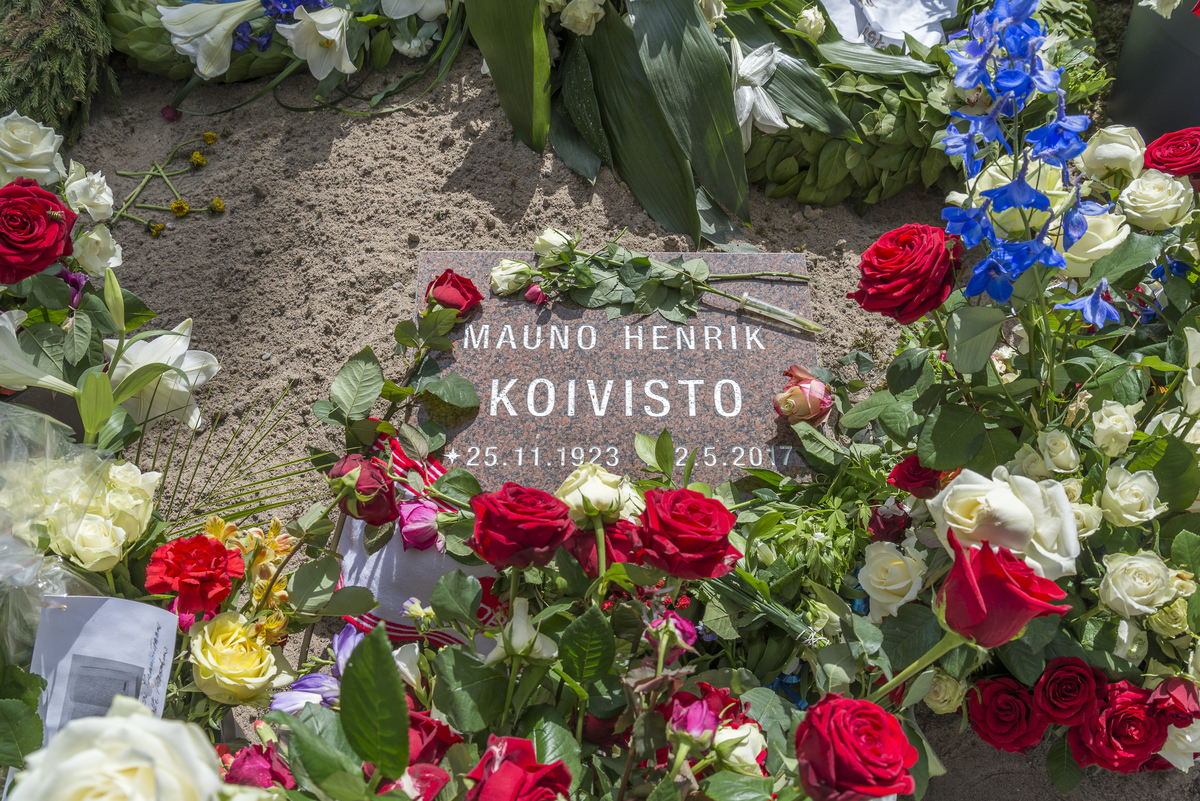 Muistolaatta presidentti Mauno Koiviston haudalla. Laattaa ympäröi ruusuja ja muita hautakukkia.