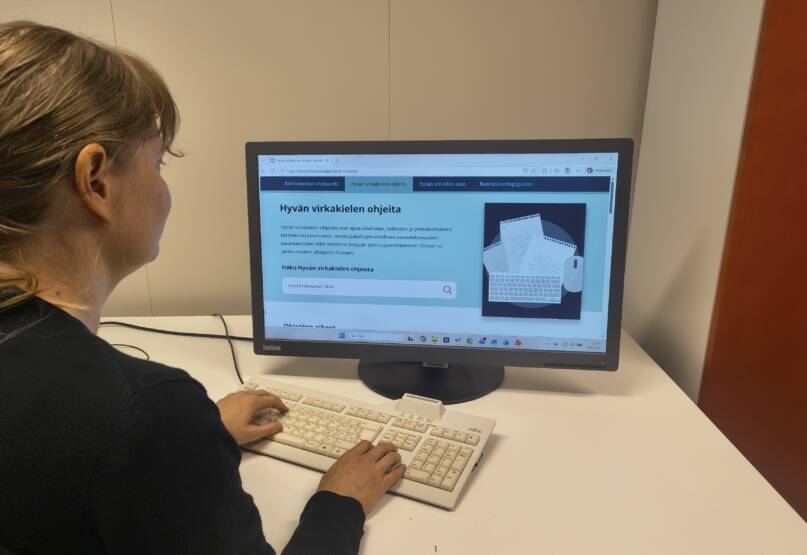 Henkilö tietokoneella, jonka ruudulla auki Hyvän virkakielen ohjeita -verkkosivu.