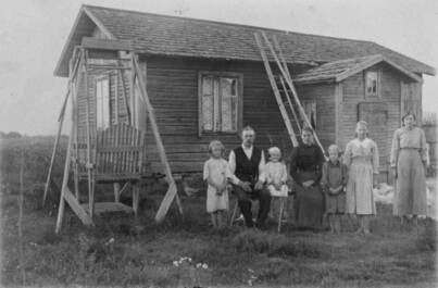 Kuvanottopaikka Vähärauma. Asuinrakennuksen edustalla keinu ja perhe ryhmäkuvassa.