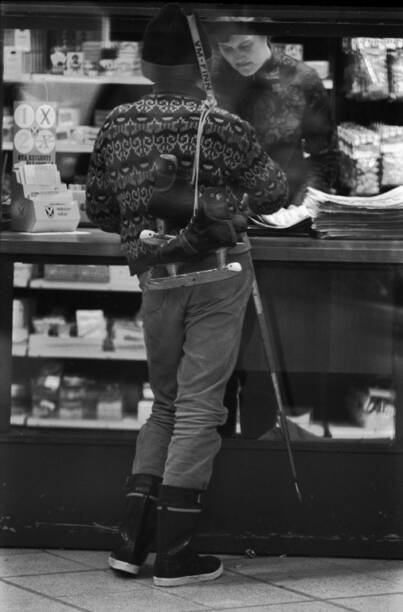 Poika kioskilla hokkarit olalla, jääkiekkomaila kädessä ja Hai-saappaat jalassa. 1970. Kuva: Simo Rista. Helsingin kaupunginmuseo. CC BY 4.0.