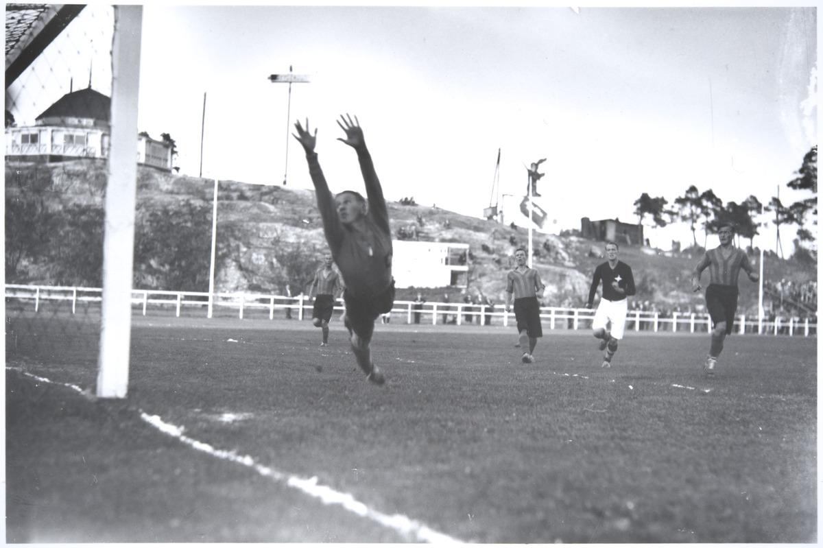 Jalkapallo-ottelu HIFK ja Helsingin Toverit Pallokentällä. Maalivahti syöksyy torjuntaan. Helsinki, elokuu 1934. Kuva: Pietinen. Museovirasto. CC BY 4.0.