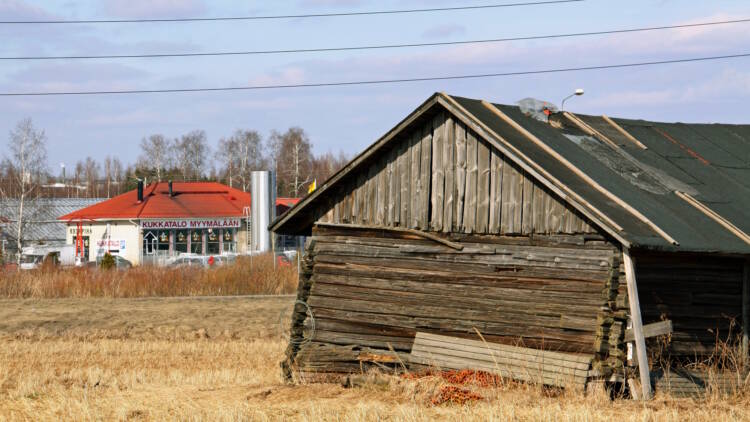 Etualalla vanha, vinossa oleva lato ja peltoa, taustalla uudempi talo, jossa kukkamyymälä.