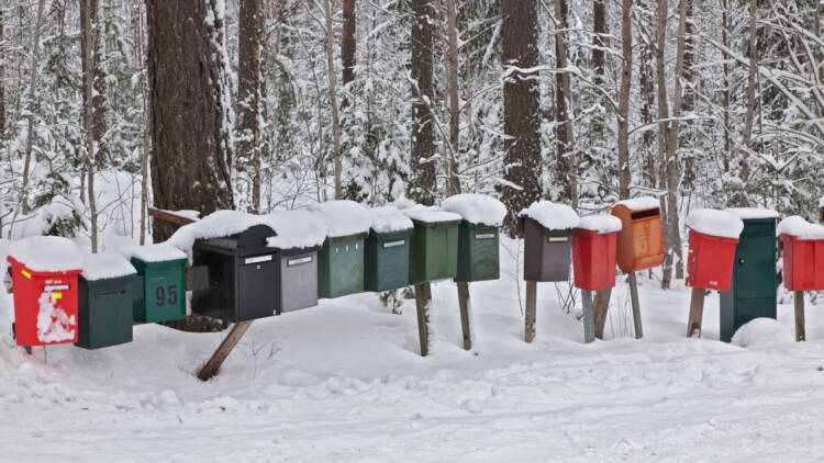 Postilaatikoita rivissä talvisessa maisemassa. Taustalla puita.