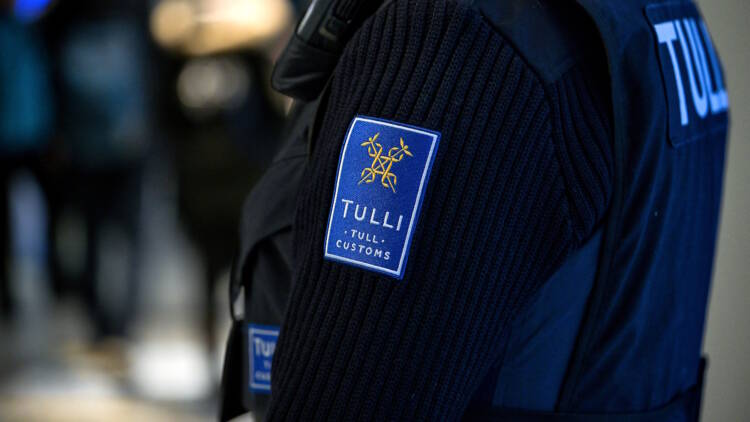 Tullitarkastaja Kittilän lentokentällä kuvattuna niin, että työasusta näkyy selkäosa ja hiha, jossa on Tullin logo.