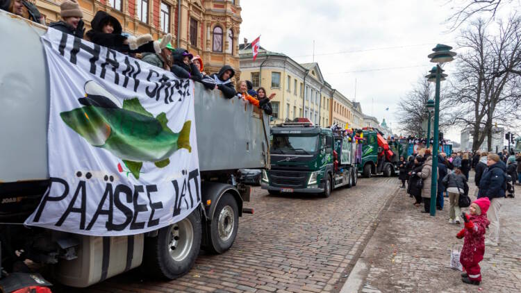 Abit matkustavat penkkariasuihin pukeutuneina kuorma-autojen lavoilla. Ihmisiä on kerääntynyt seuraamaan ajelua.